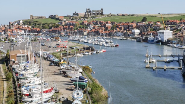 Un port où de nombreux bateaux sont amarrés, un bâtiment historique en arrière-plan et une ville avec des maisons aux toits rouges.