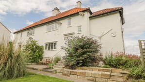 A two-story house with a red-tiled roof, white walls, and a stone staircase leading to the front door. - Stakesby House Apartment 3 (Whitby)