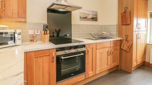 A modern kitchen with wooden cabinets, a built-in oven, a microwave, and a stainless steel range hood. - Stakesby House Apartment 3 (Whitby)
