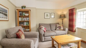A cozy living room with a grey sofa, a wooden coffee table, and a bookshelf filled with books. - Stakesby House Apartment 3 (Whitby)