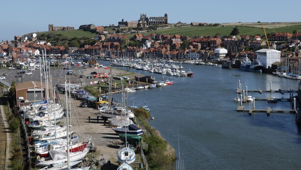 A marina with boats docked, a town in the background, and a hill with a castle-like structure. - Stakesby House Apartment 3 (Whitby)