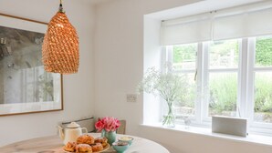 Ett runt träbord med ett fat fullt av bakverk, en tekanna och en vas med blommor.