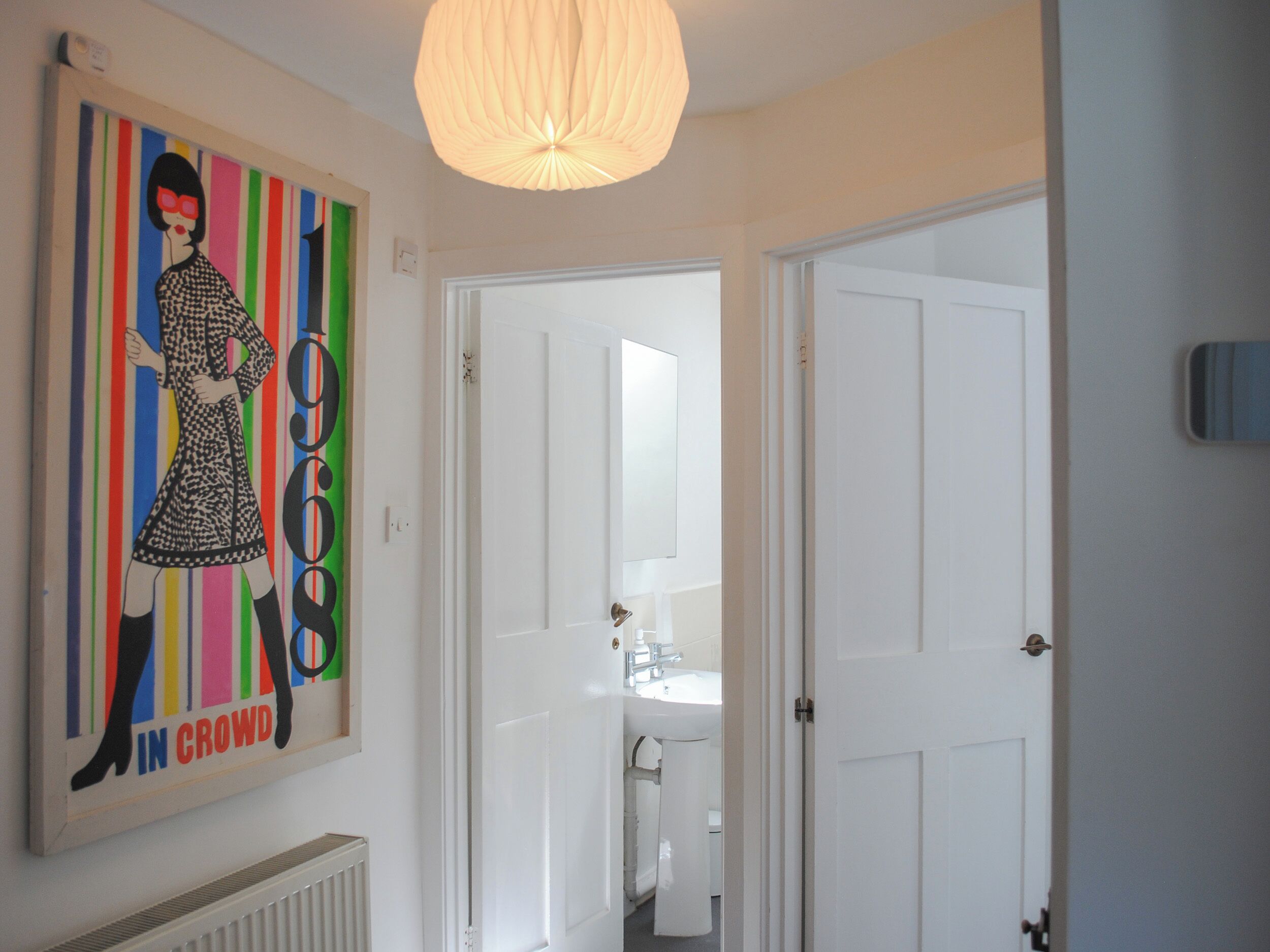 En gang med et billede i ramme på væggen, en hvid dør og en loftlampe.