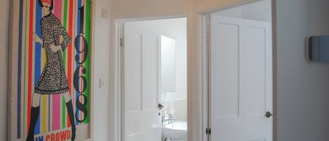 A hallway with a framed artwork on the wall, a white door, and a ceiling light fixture.
