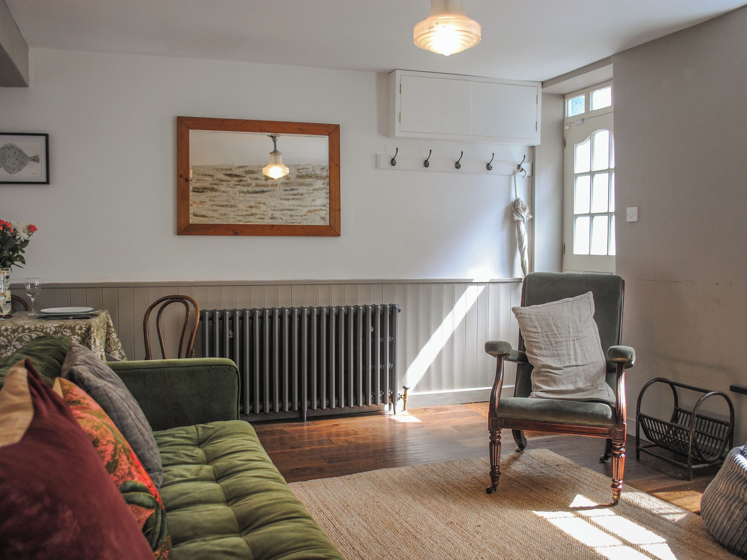 Una sala de estar acogedora con un sofá verde, una silla de madera, un radiador y una obra de arte enmarcada en la pared.