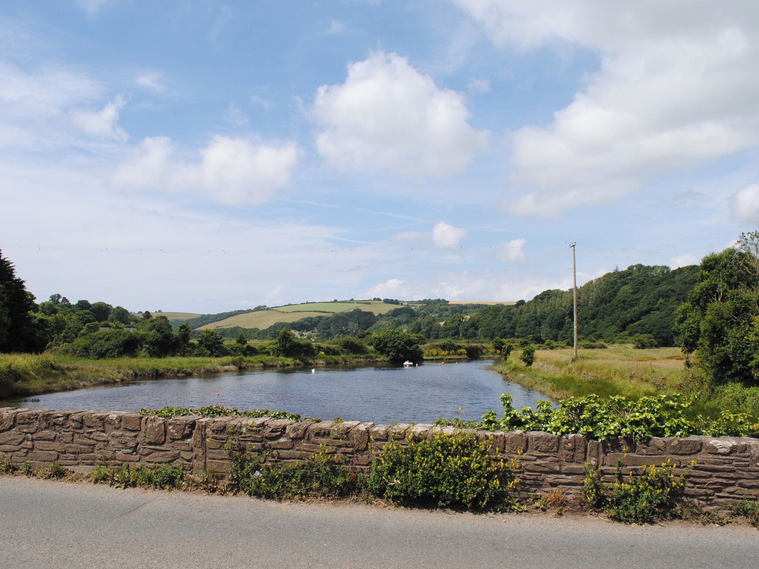 A rural landscape with a stone wall, a river, and rolling hills.