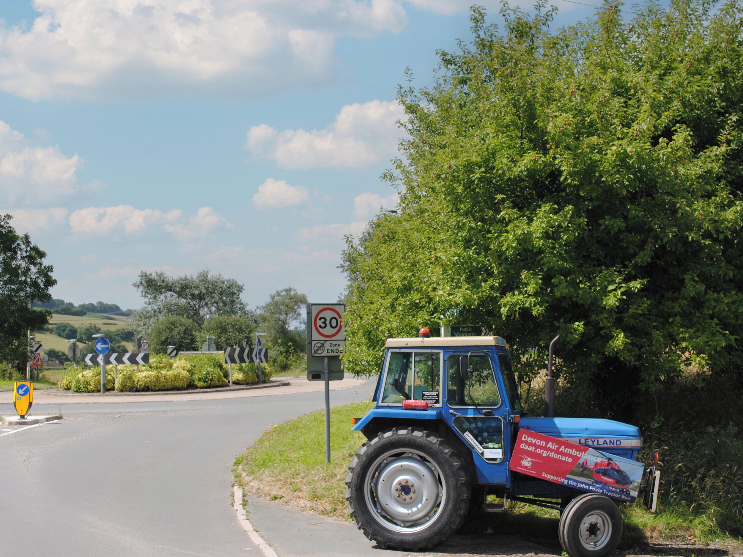 Un tracteur bleu est garé sur une route de campagne, à proximité d’un panneau indiquant une limitation de vitesse à 30.