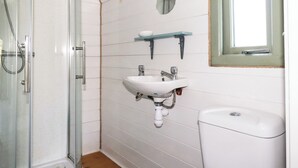 A bathroom with a glass shower enclosure, a white sink with a mirror above it, and a toilet. - The Lamb Shack (Bodmin)