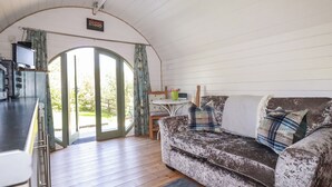 A cozy room with a sofa, a small table with a chair, and a kitchen area with a counter and appliances. - The Lamb Shack (Bodmin)