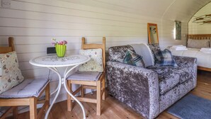 A cozy room with a wooden floor, a round table with chairs, a sofa with patterned cushions, and a bed with pillows. - The Lamb Shack (Bodmin)