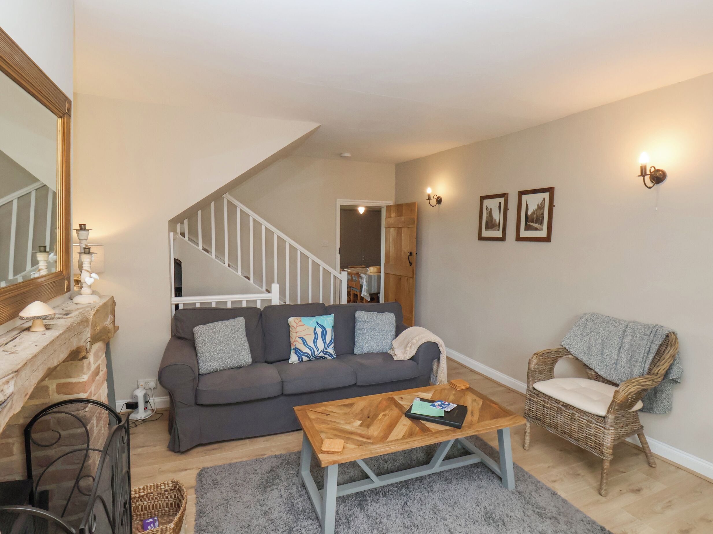 Een woonkamer met een grijze bank, een houten salontafel, een rieten fauteuil en een open haard.