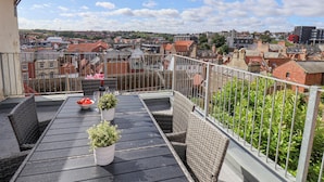 Ein Balkon mit Tisch und Stühlen, Topfpflanzen und Blick auf eine Stadtlandschaft.