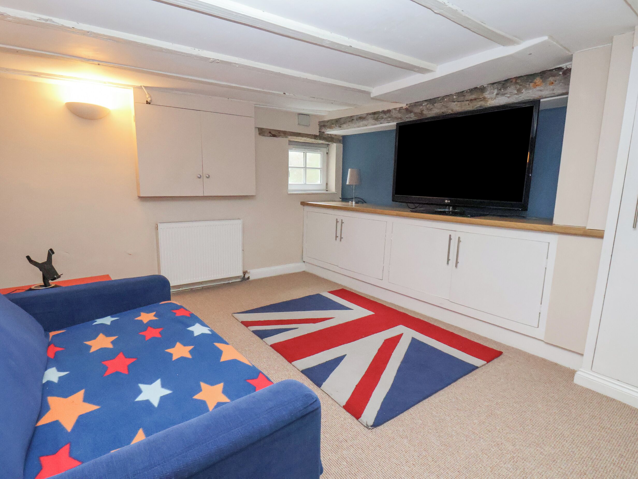 Et værelse med en blå sofa, hvide skabe, et fladskærms-tv og en måtte med Union Jack.