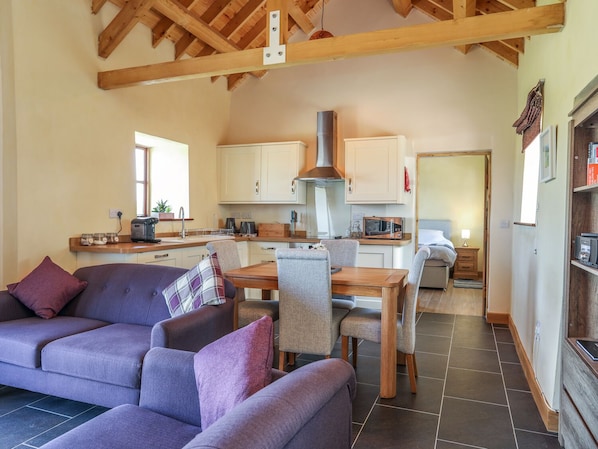 A cozy living room with a sofa, chairs, and a dining table. There is a kitchen area with cabinets and appliances.