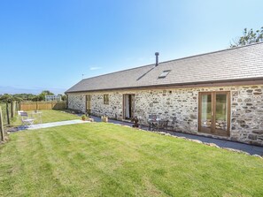 A stone building with a sloped roof, a fenced backyard, and a clear sky.