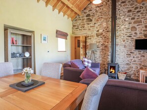 A cozy living room with a stone wall, a fireplace, a wooden dining table, and comfortable seating.
