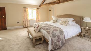 A bedroom with a large bed, a bench, a nightstand, and a window with curtains.