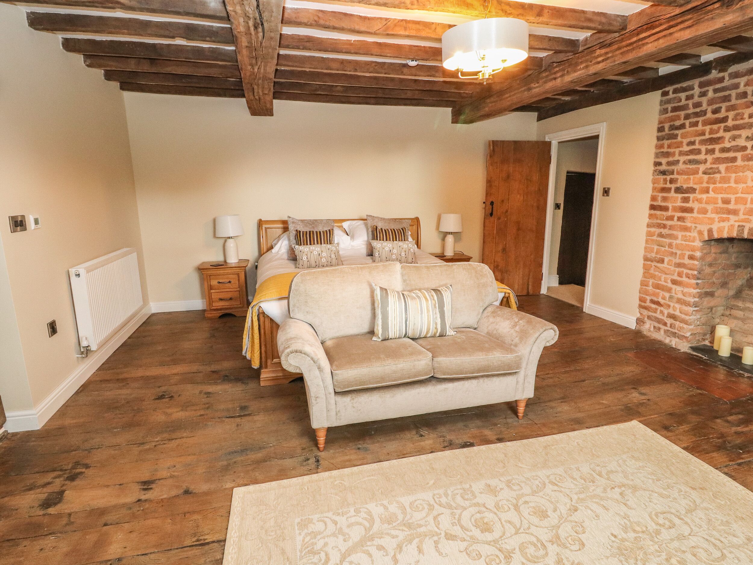 A bedroom with a wooden ceiling, a bed with multiple pillows, a nightstand, a lamp, a fireplace, and a radiator.