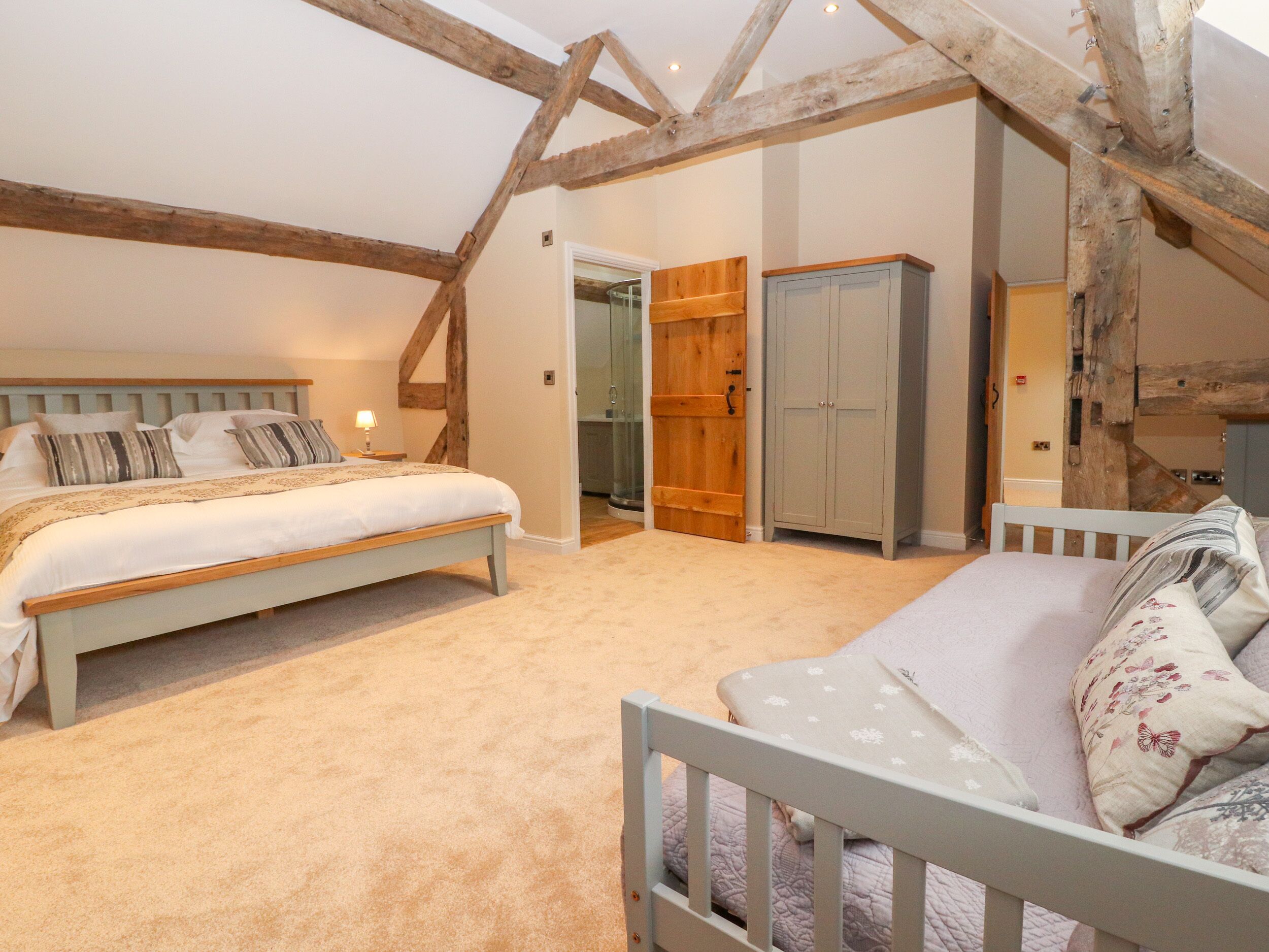 A bedroom with a bed, a crib, a wardrobe, and a door leading to another room.