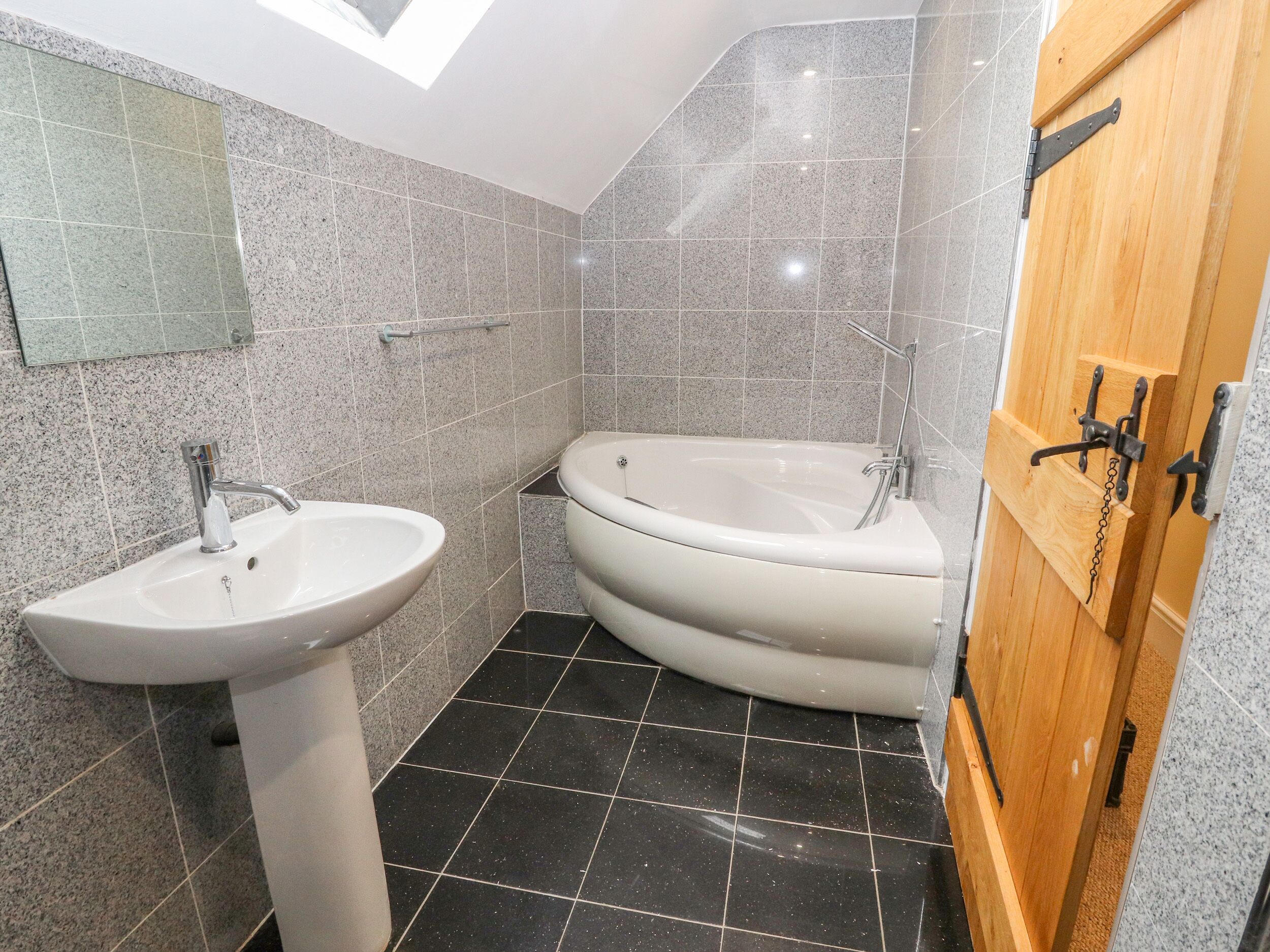 A bathroom with a freestanding bathtub, a pedestal sink, and a wooden door with a metal handle.