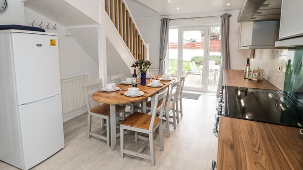 A modern kitchen with a dining area, white cabinetry, a built-in oven, and a staircase.