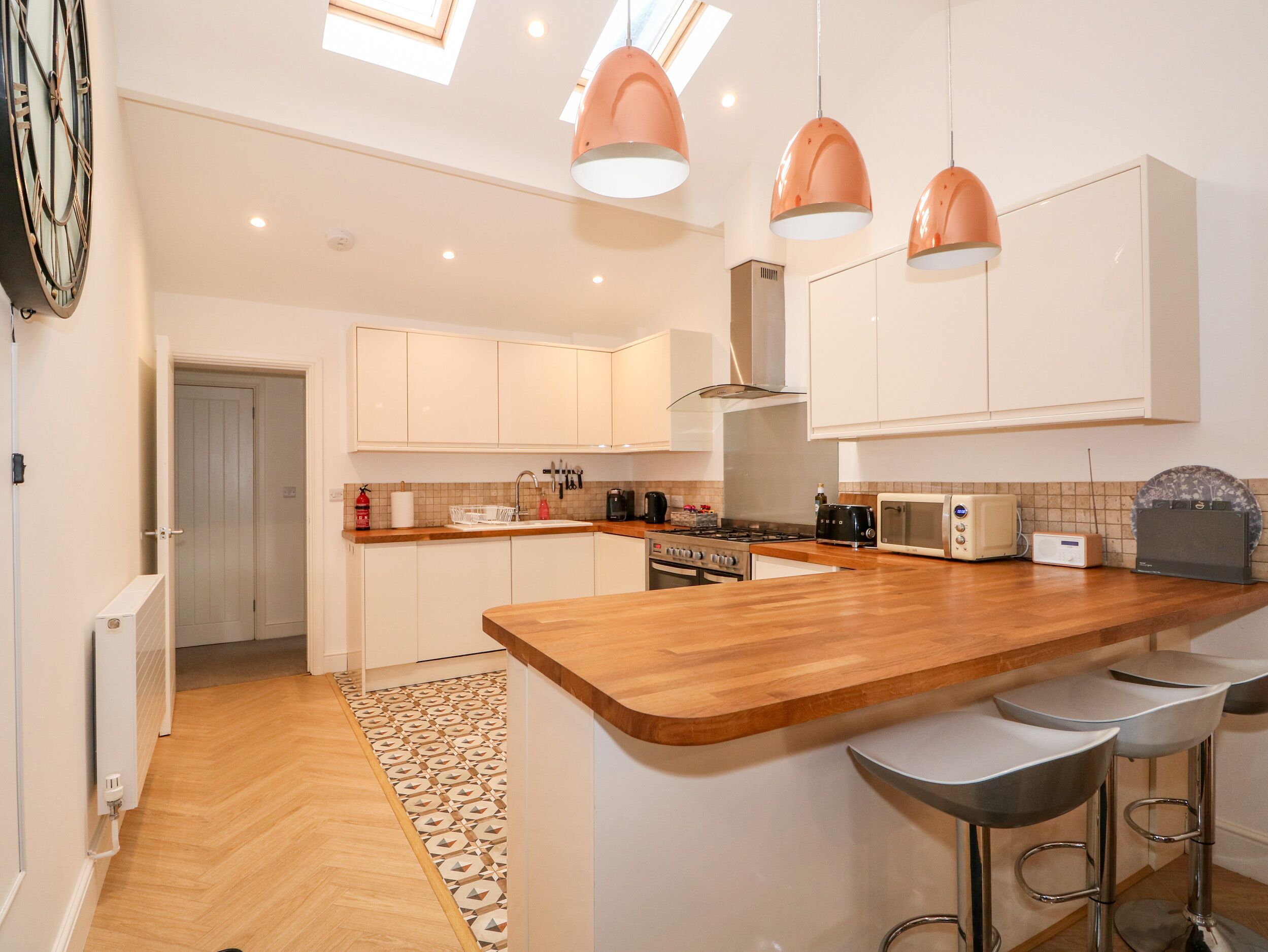 Une cuisine moderne dotée d’un îlot central en bois, d’appareils électroménagers en acier inoxydable, de luminaires suspendus et d’un tapis à motifs.