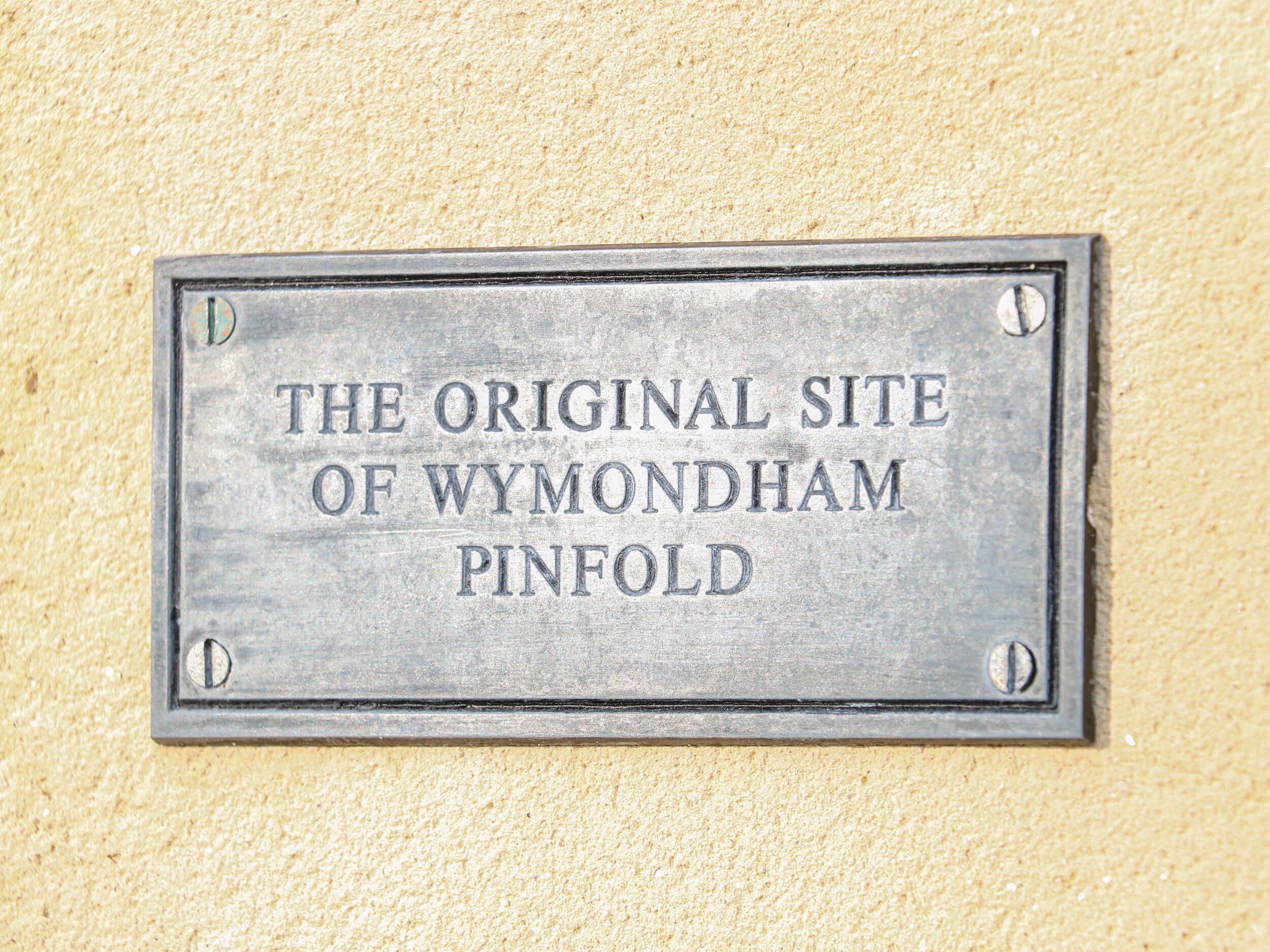 Una placa de metal con la inscripción 'THE ORIGINAL SITE OF WYMONDHAM PINFOLD'.