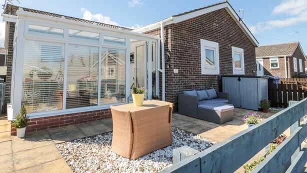 A residential property with a glass conservatory, a patio with outdoor furniture, and a brick house. - The Snug (Chathill)