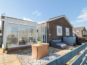 Una propiedad residencial con un invernadero de vidrio, un patio con muebles de exterior y una casa de ladrillo.