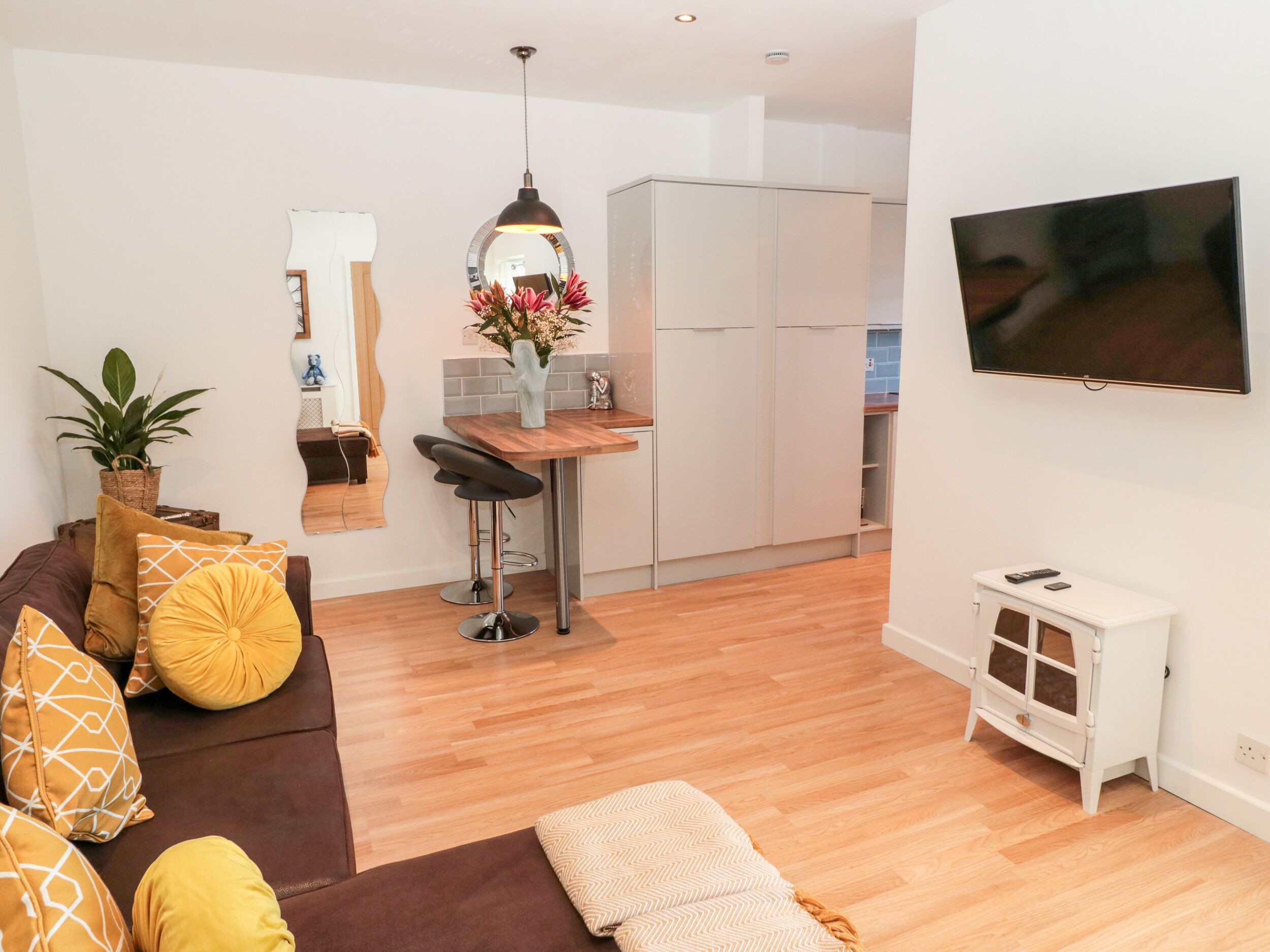 A modern living room with a brown sofa, yellow cushions, a wooden coffee table, and a TV mounted on the wall.