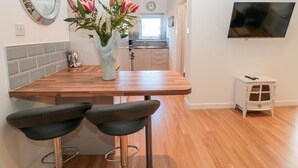 A modern kitchen with a wooden countertop, two bar stools, a vase with flowers, a mirror, and a TV on the wall. - The Snug (Chathill)