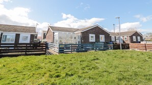 A row of brick houses with a grassy field in the foreground. - The Snug (Chathill)