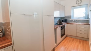 A modern kitchen with white cabinets, a microwave, a sink, and a clock on the wall. - The Snug (Chathill)