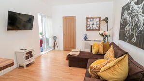 A modern living room with a brown sofa, a flat-screen TV, and a wooden floor. - The Snug (Chathill)