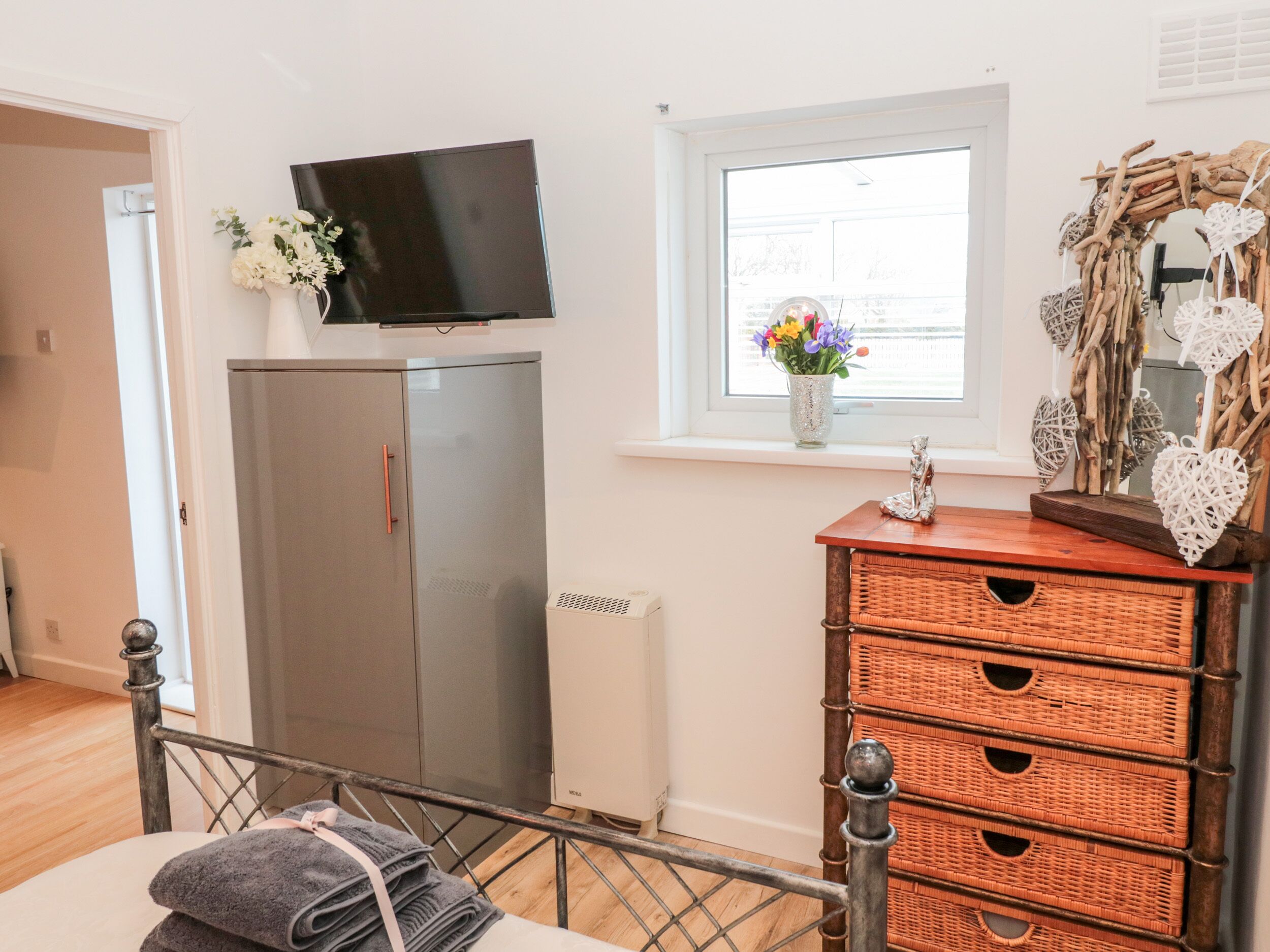 A bedroom with a bed, a dresser, a television, and a window with flowers.