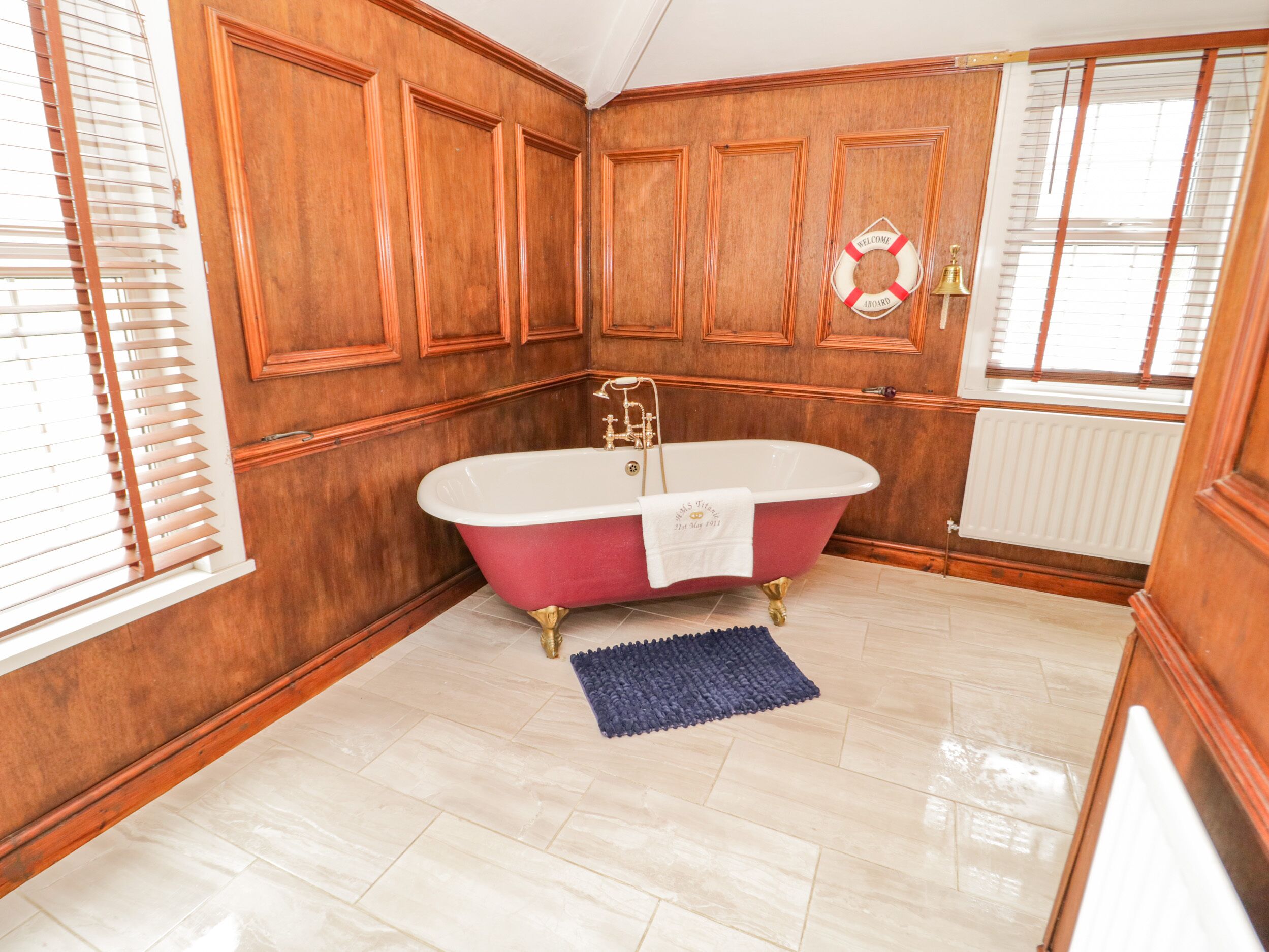A bathroom with a freestanding bathtub, wooden paneling, a blue rug, and a welcome sign.