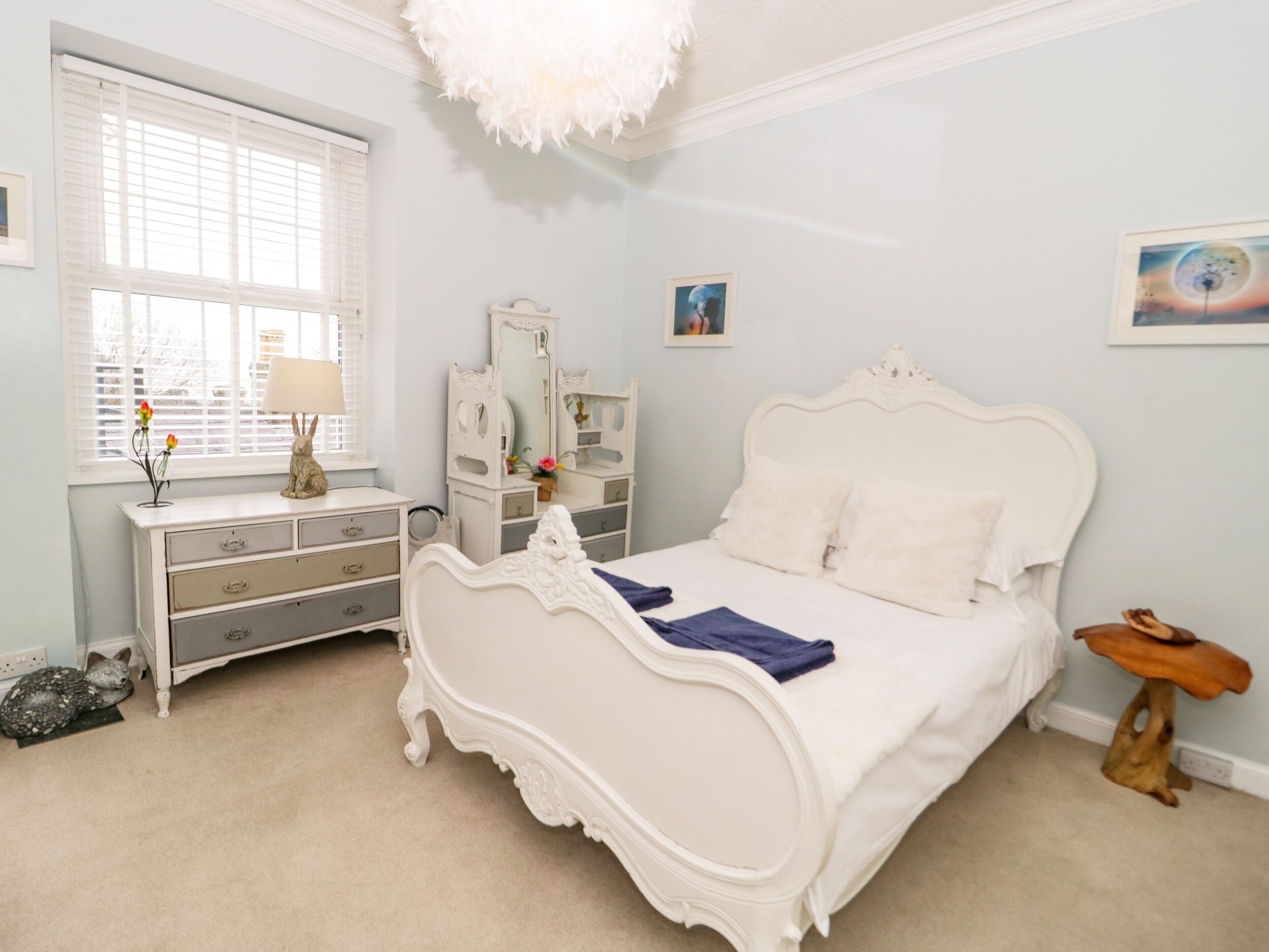 Un dormitorio con una cama blanca ornamentada, un aparador, un tocador con espejo y una ventana con persianas.