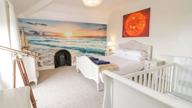 Un dormitorio con un mural de una puesta de sol sobre el océano, un telescopio y una cuna.