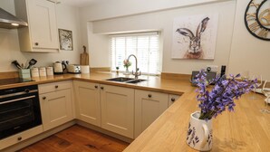 Une cuisine moderne avec des meubles en bois, un four encastré, un évier et une fenêtre équipée de stores.