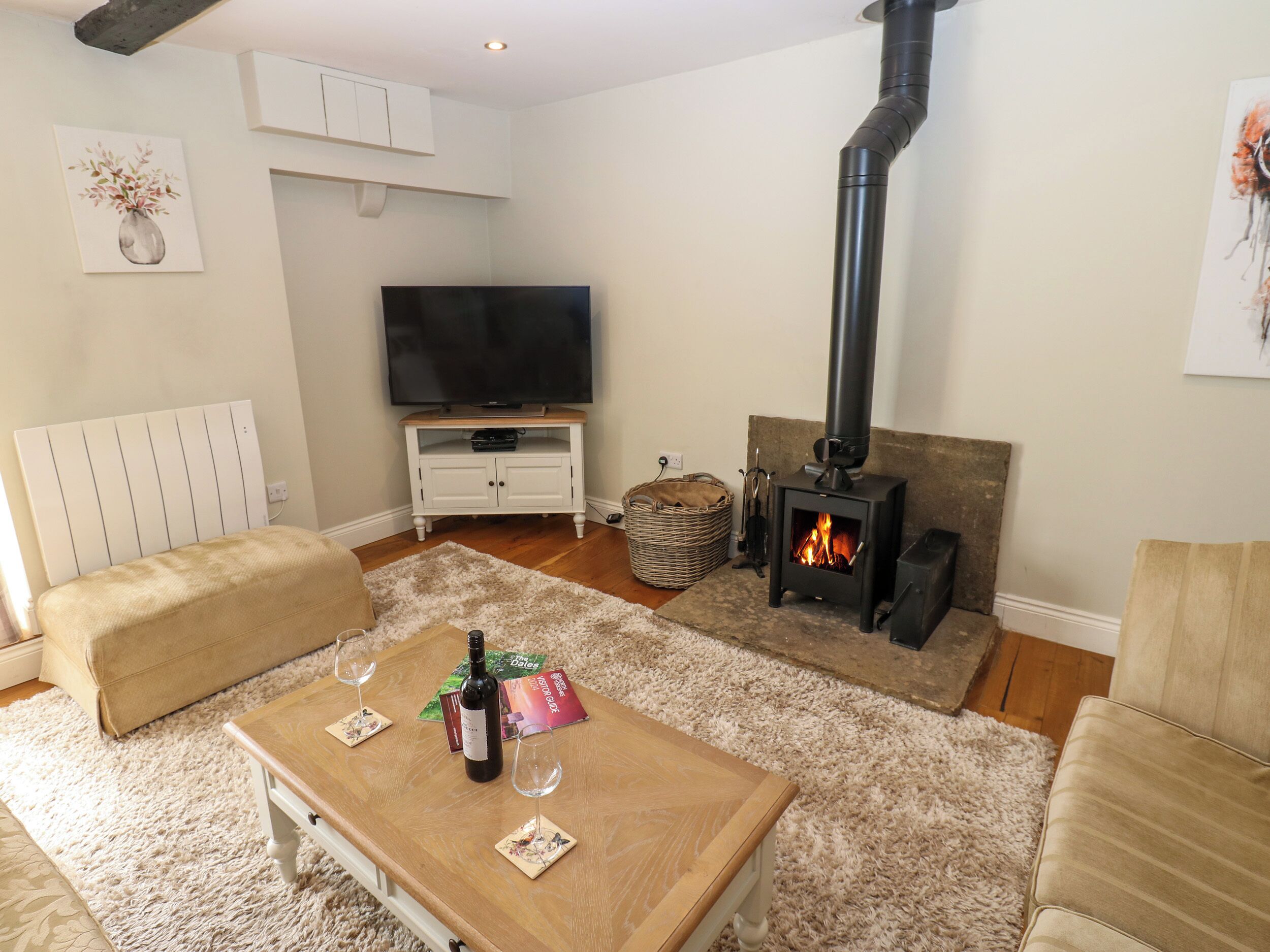 A living room with a sofa, a coffee table with a bottle and glasses, a TV, a fireplace, and a white cabinet.