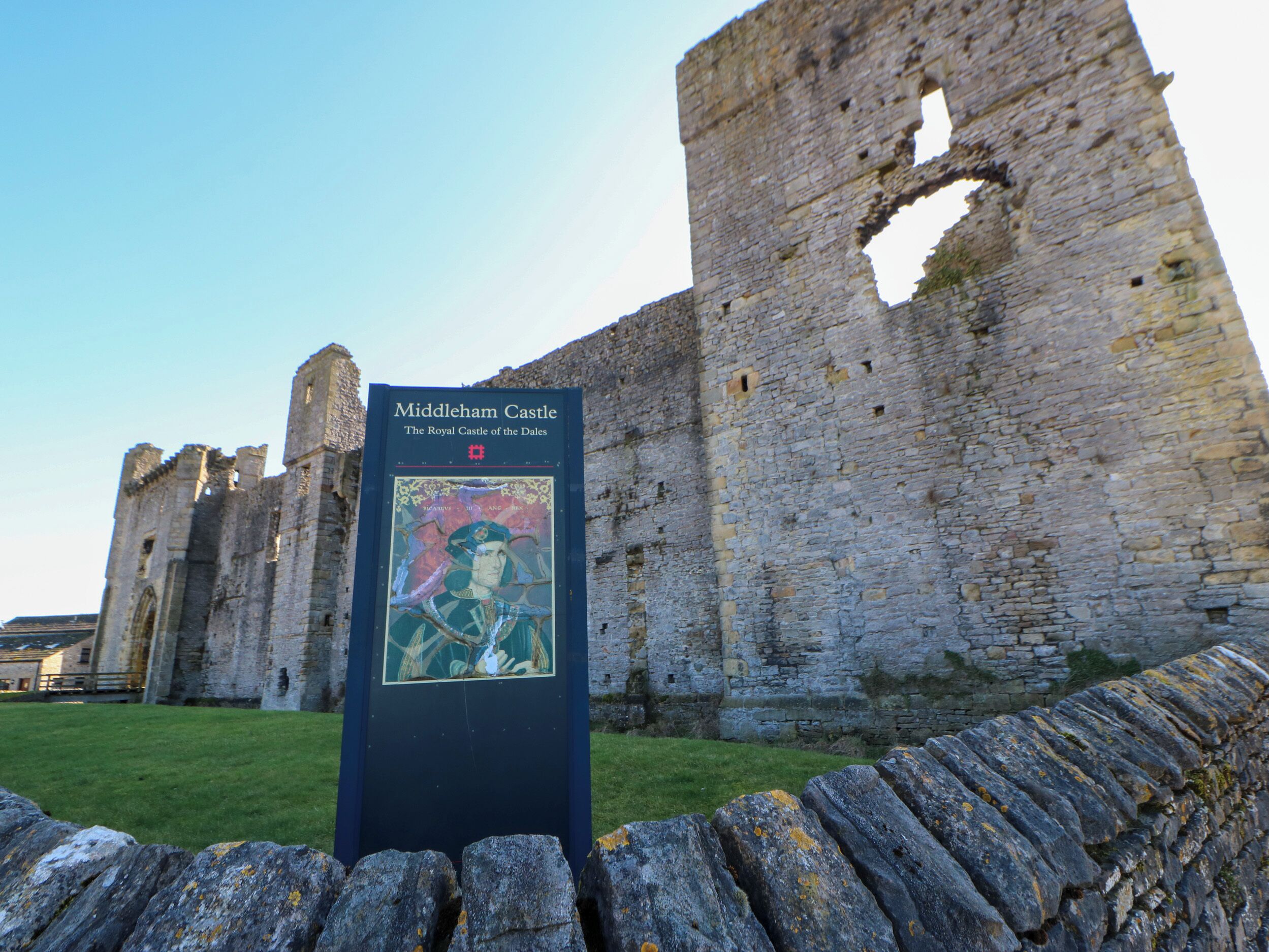 Castillo de Middleham con un cartel histórico y muros de piedra.