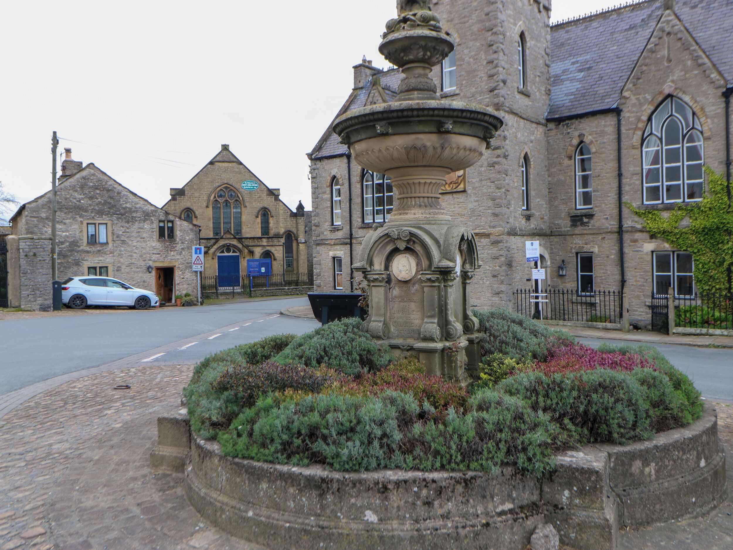 A stone fountain with inscriptions in front of a historic building with arched windows and a blue door.