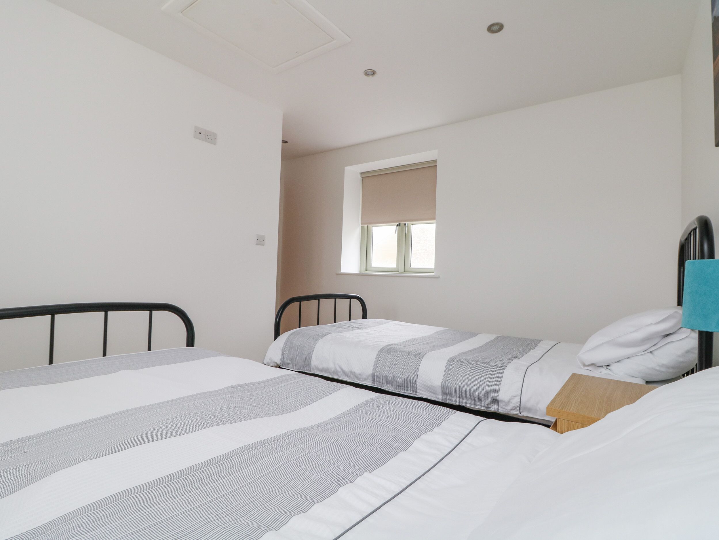 Ein kleines, schlichtes Zimmer mit zwei Einzelbetten, einem Fenster mit Jalousie und einer schlichten weißen Wand.