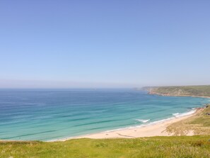 A coastal landscape with a beach, grassy areas, and a clear sky.