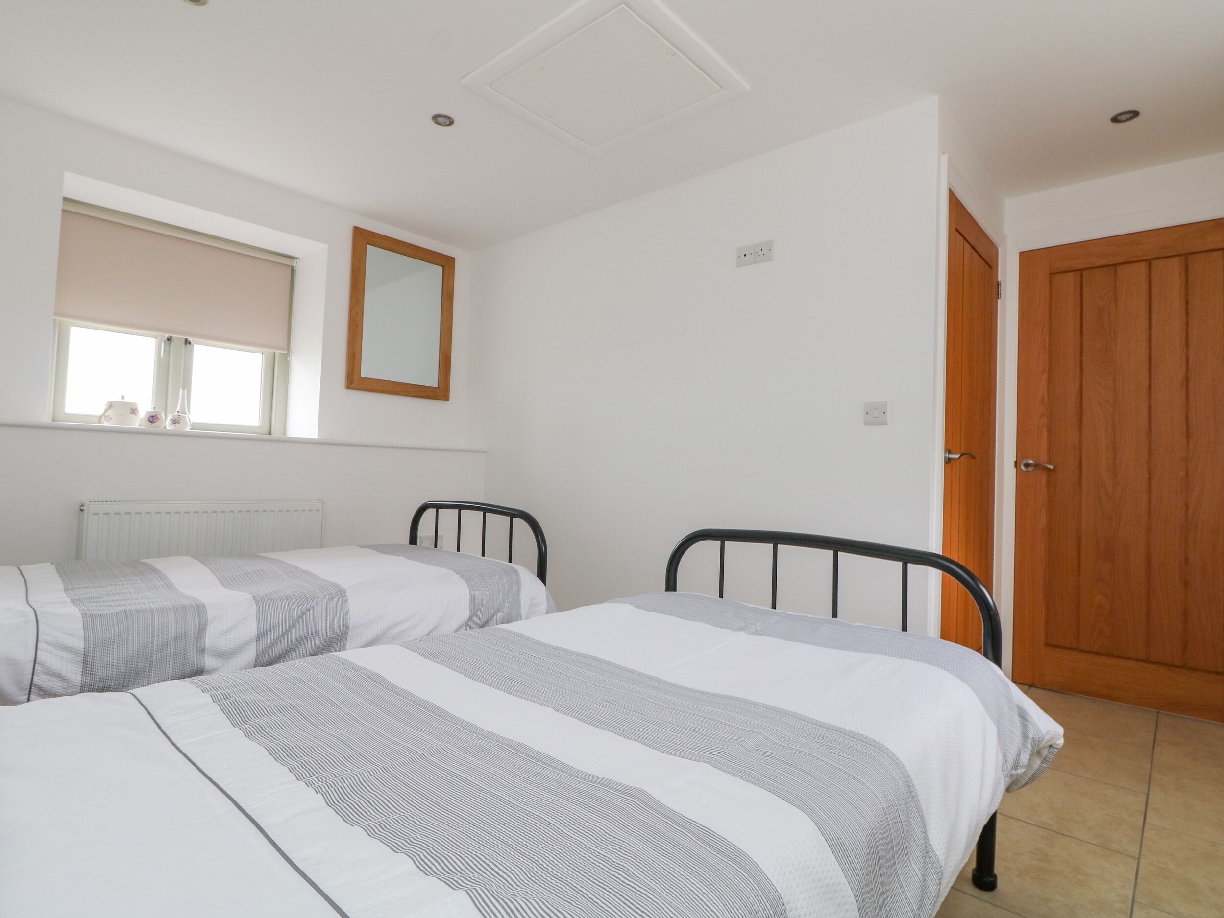 A bedroom with two beds, a window with a blind, a mirror, and a wooden door.
