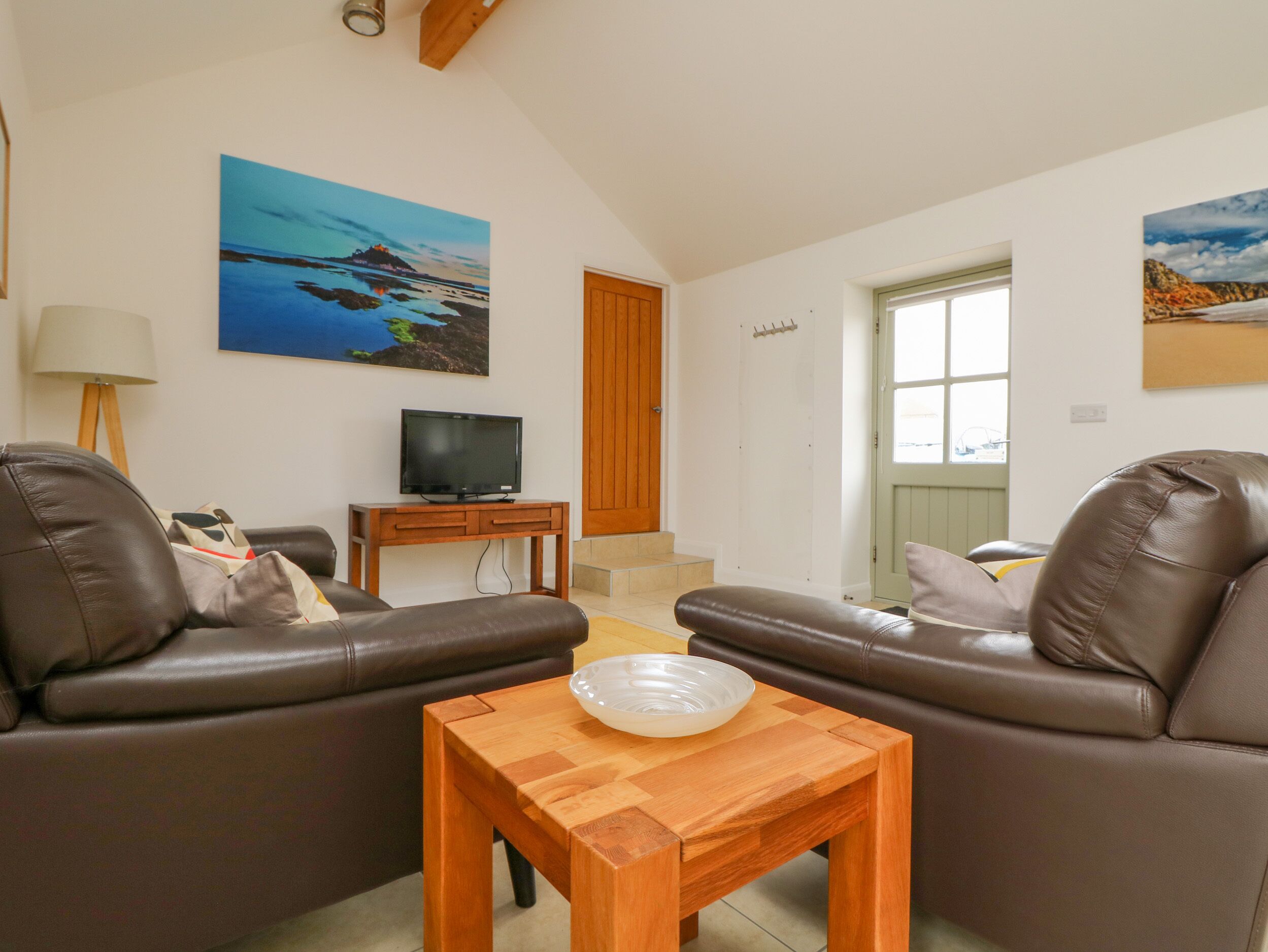 Uma sala de estar com dois sofás de couro, uma mesa de centro de madeira, uma televisão sobre um móvel e um quadro na parede.
