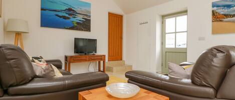 A living room with two leather sofas, a wooden coffee table, a television on a stand, and a painting on the wall.