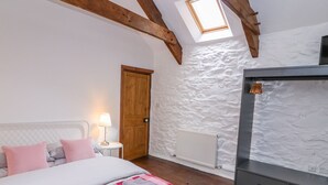 Ein Schlafzimmer mit Bett, Nachttisch, Lampe, Holztür, Heizkörper und einer geneigten Decke mit Dachfenster.