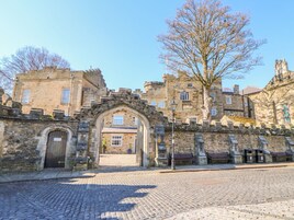 Un edificio histórico de piedra con un amplio arco de entrada, un patio empedrado y un árbol en primer plano.