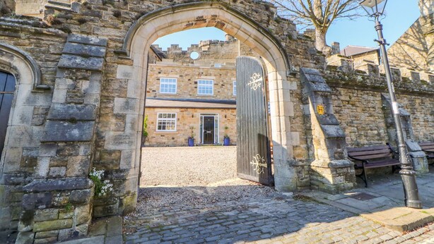 An entrance to a historic building with a stone archway, a wooden door, and a gravel path leading to a building with windows and a door. - Castle Keep at Stanhope Castle (Bishop Auckland)